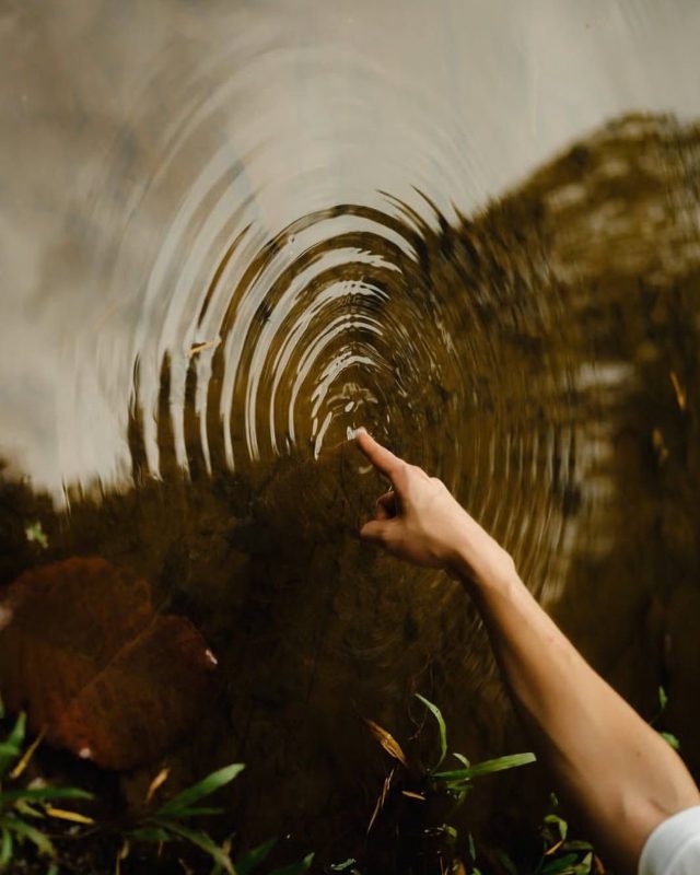 A hand moves through water, leaving rings behind