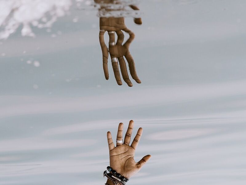 Two hands reaching through a reflection in water